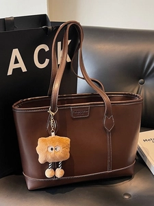 Sac cabas en cuir marron avec surpiqûres et breloque peluche sur canapé noir
