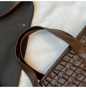 Detailed close-up of woven dark coffee leather texture and cylindrical handle stitching