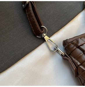 Macro detail of brown woven bucket bag featuring silver lobster clasp and leather strap
