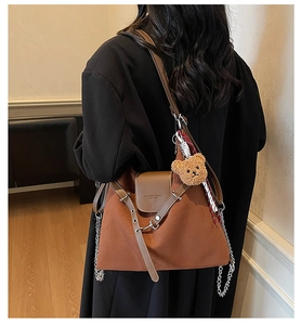 Detail of brown matte leather tote bag with chain strap and teddy bear charm on model