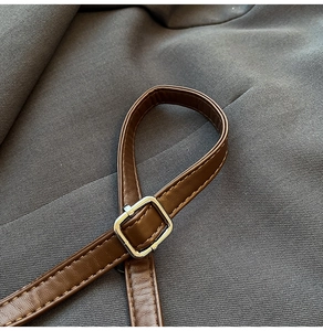 Macro detail of brown leather shoulder strap with a silver metal square buckle fastener