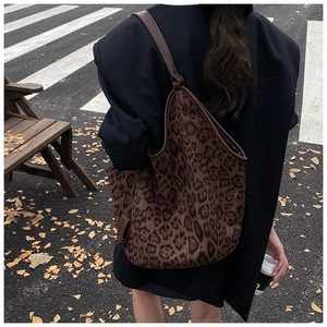 Detailed view of leopard print tote bag with brown leather straps in an autumn street setting