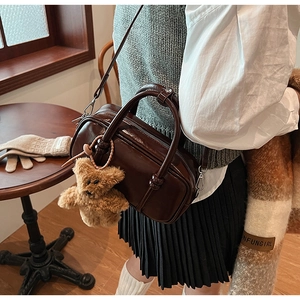 Detail of dark brown leather bowling bag with a cute plush bear pendant accessory