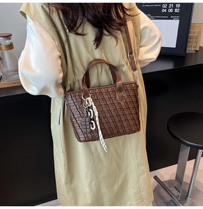 Detail of dark brown woven tote bag with leather handles and a chocolate charm pendant