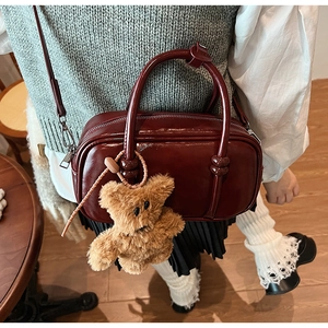 Close-up of vintage burgundy shoulder bag with shiny PU leather and cute bear charm