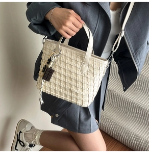 Detail view of cream woven bucket bag with chocolate charm on a person in soft light