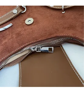 Detail of smooth silver zipper and stitching on a brown suede tote bag
