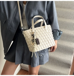 Detail of off-white woven tote bag with chunky chain and chocolate bar charm pendants