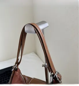 Detail of brown tote bag showing contrast stitching on straps and silver metal hardware