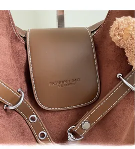 Detail of dark brown tote bag with white stitching, leather logo, and plush charm
