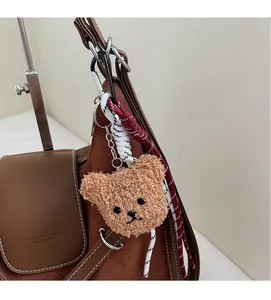 Close-up of fluffy brown bear charm with braided rope hanging on a brown suede tote bag