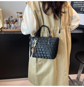 Detailed view of black woven bucket bag with chocolate pendant and slim shoulder strap