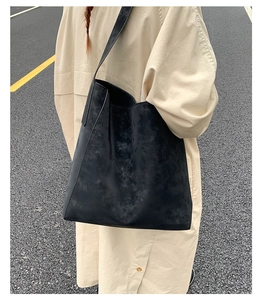 Dettaglio di una grande borsa tote in pelle scamosciata nera su un trench beige moderno