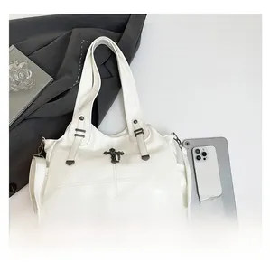 Macro detail of white patent leather tote bag featuring a vintage metal cross ornament