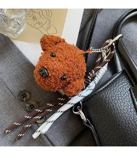 Brown teddy bear plush charm with metallic buckle and woven rope on black leather bag