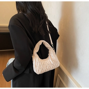 Detail view of quilted beige underarm bag with crystal accents on a model in a black blazer