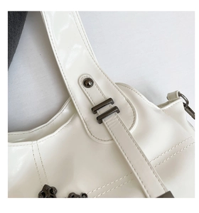Detailed close-up of white leather tote bag showing gunmetal rivets and gothic cross charm