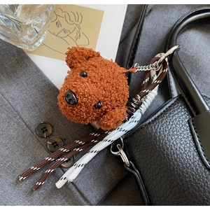 Close-up of a brown teddy dog plush charm hanging on a textured black leather bucket bag