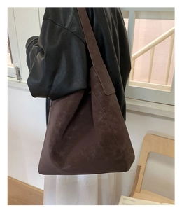 Grande borsa tote in pelle scamosciata marrone scuro indossata da modella in un caffè