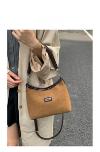 Detail of tan suede shoulder bag featuring dark leather handles and metal hardware