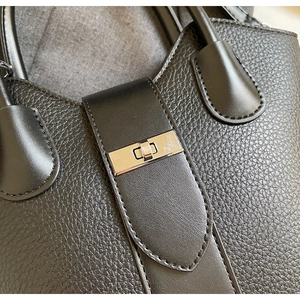 Detail of black lychee grain leather handbag featuring a polished silver metal twist lock