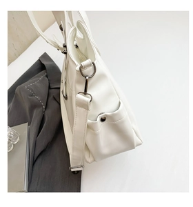 Macro detail of a white leather tote bag featuring metal rivets and adjustable straps