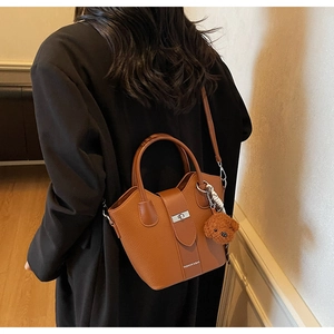 Detail view of brown bucket bag with silver metal twist lock and cute bear charm