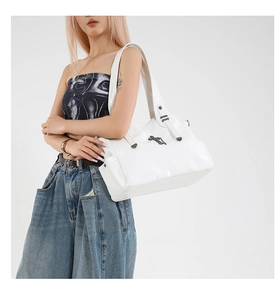 Detailed view of white patent leather tote bag with metallic cross emblem and glossy finish