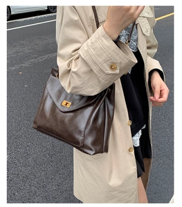 Detail of a large dark brown tote bag featuring a gold rectangular twist lock on the flap