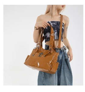 Detail view of brown patent leather tote bag with silver cross pendant and chain accent