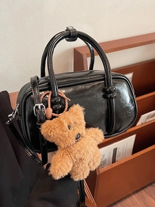 Chic black patent leather bowling bag with brown plush bear charm and adjustable strap