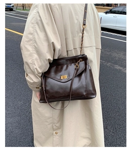 Detail of dark brown glossy leather shoulder bag with gold chain and metal twist lock