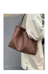 Close-up of deep brown woven leather tote bag texture on model shoulder in outdoor setting