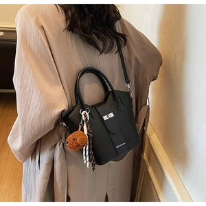 Detail of black lychee grain leather bucket bag with silver clasp and plush bear charm