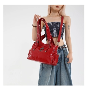 Detail of red glossy patent leather tote bag with vintage metal cross pendant