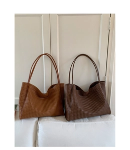 Detailed view of woven leather tote bags in caramel and dark coffee colors on a soft surface