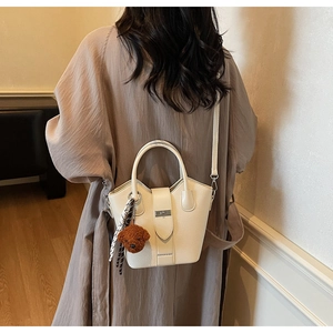 Detail of cream bucket bag with bear pendant and polka dot scarf shown on a model