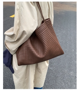 Detail of dark brown woven tote bag worn with a classic trench coat in an urban street setting