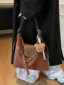 Brown suede tote bag with chain strap and teddy bear charm shown on shoulder