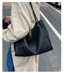 Outdoor street style shot of a large black woven tote bag worn with a chic trench coat