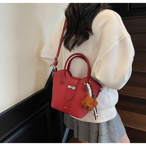 Red lychee grain leather bucket bag with bear charm and decorative scarf detail