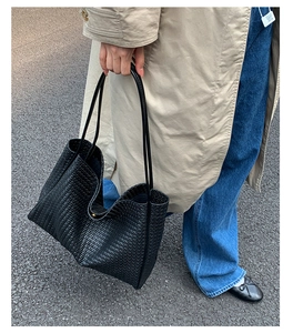 Detail of black woven texture tote bag worn with a beige trench coat on a city street