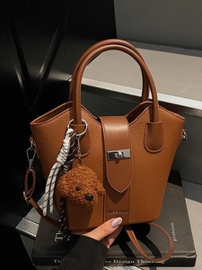 Brown lychee leather bucket bag with top handle and teddy bear charm on book background