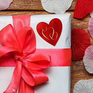 Detail of red heart sticker with gold outline on a gift box with a red satin bow