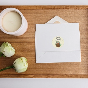 Round Happy Easter stickers with egg basket on white envelope over a wooden tray