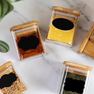 Close-up of glass spice jars with bamboo lids and black waterproof labels on marble