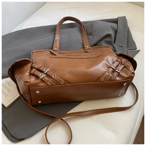 Detail of brown PU tote bag showing metal buckles, straps, and protective bottom studs