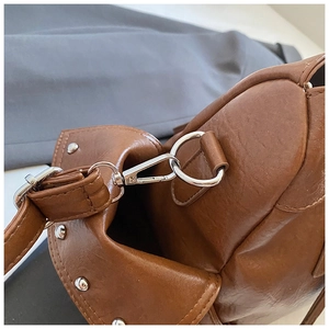 Detail view of caramel leather bag featuring silver D-rings and studded metal accents