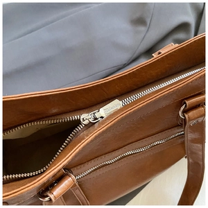 Detail of brown glossy leather bag featuring vintage texture and silver engraved zipper