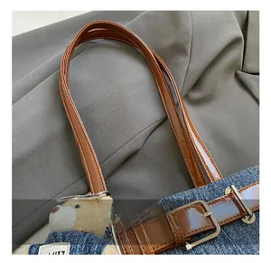 Detail der blauen Jeans-Umhängetasche mit braunem Lederriemen und Plüschbär-Anhänger